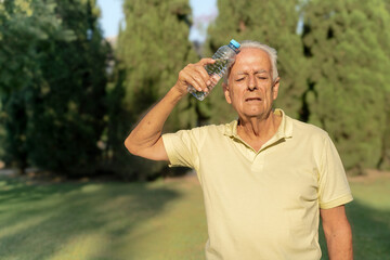 Elderly man placing cold water bottle on forehead to relieve heat stroke symptoms during summer heat