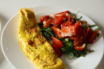 Healthy breakfast with omelette and fresh salad with cherry tomatoes and arugula, dressed with mustard, honey and olive oil sauce on white plate. Nutritious meal with protein and fiber. Ketogenic diet