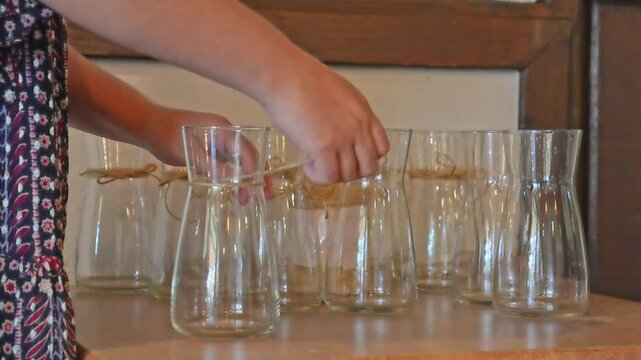 Skilled florist carefully preparing empty glass vases, wrapping decorative jute twine around their delicate necks within rustic workshop setting