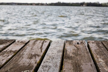 Obraz premium Weathered wooden dock extends into a serene lake, offering a tranquil view of the rippling water. Perfect for evoking relaxation, nature's beauty, and a sense of peace.