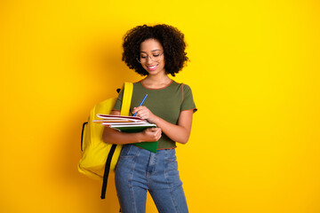 Attractive young woman with curly hair studying while holding notebooks and a pen against a vibrant...