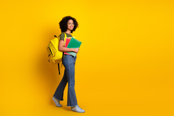 Cheerful teenage girl smiling with book and backpack on a vibrant yellow background