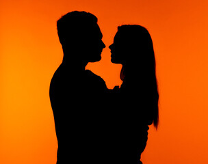 Silhouette of Couple Embracing Against Vibrant Orange Background