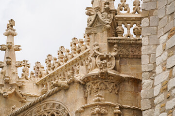 Detailed stone carvings adorn a building's facade. Gothic architecture features intricate sculptures, ornate details, and a weathered stone texture against a cloudy sky. © KetteCreate