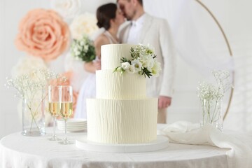 Happy married couple together indoors, focus on wedding cake and glasses of champagne on table
