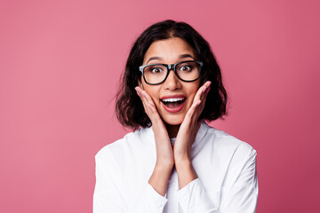 Excited young woman in glasses expressing enthusiasm and joy against a vibrant pink background in...