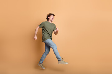 Energetic young man in casual outfit smiling and walking joyfully against a beige background