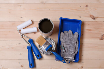 Painting tools, rollers, brush, gloves, and open can of finish are neatly arranged on wooden floor,...