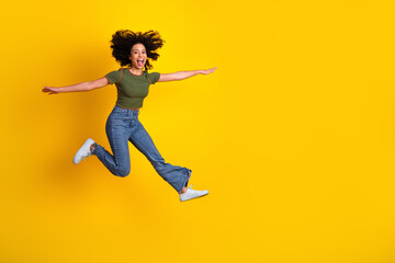 Energetic young woman leaping joyfully against a vibrant yellow background, showcasing happiness...