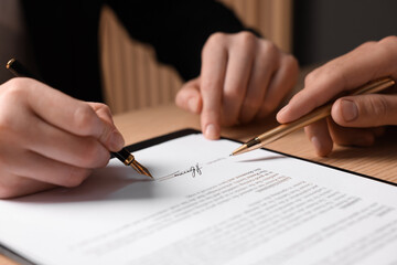 Man pointing at document and woman putting signature at table, closeup
