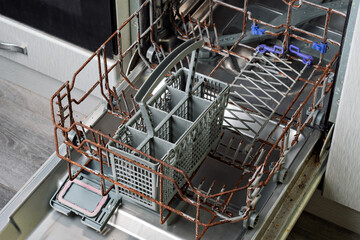 Protective coating of dishwasher rack has cracked and peeled, exposing rusted metal and causing deterioration of the basket frame, symbolizing appliance wear.