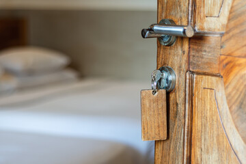 Old wooden hotel room door with metal handle and classic key tag slightly open, revealing simple bed and evoking nostalgic hospitality vibes.