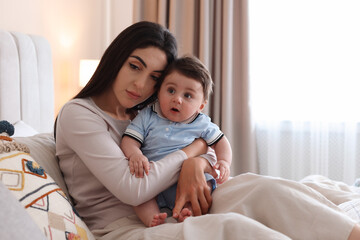 Woman suffering from postpartum depression with her little baby on bed at home