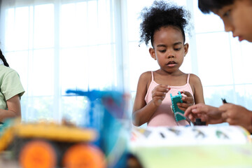 A young girl with dark curly hair is deeply focused on assembling a colorful construction toy,...