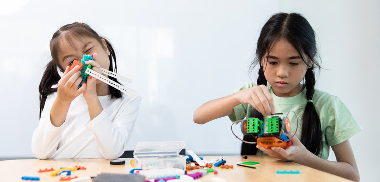 Two young girls are engaged in a STEM activity, building and exploring with colorful robotics kits at a table, fostering hands-on learning.