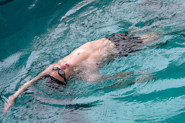 Asian male swimmer swimming backstroke in pool