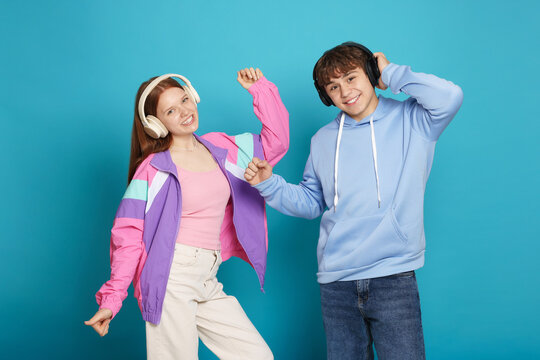 Fototapeta Teenage girl and boy with headphones dancing on light blue background