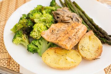 Delicious dish of fried river trout fillet with garnish of broccoli, asparagus sprouts, baked potatoes and mushroom sauce