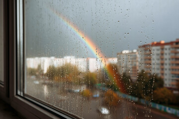 Rainbow View: A vibrant rainbow seen through a rain-streaked window over the city.