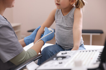 Sonographer conducting ultrasound examination of little girl's arm in clinic, closeup