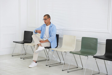 Man looking at wristwatch while waiting for appointment indoors