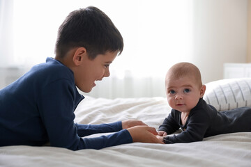 Cute little brothers holding hands on bed at home