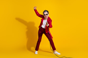 Energetic senior woman in vibrant red clothing singing with a microphone against a bright yellow background