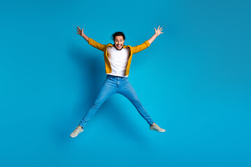 Fototapeta premium Energetic young man in casual attire jumping playfully against a vibrant blue background, expressing joy and style