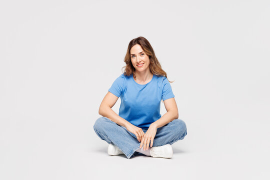 Full body young smiling happy cheerful fun Caucasian woman wears blue t-shirt casual clothes sit looking camera isolated on plain solid white color wall background studio portrait. Lifestyle concept.