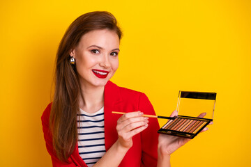 Elegant young woman applying makeup with a palette while smiling, surrounded by style and glamour...
