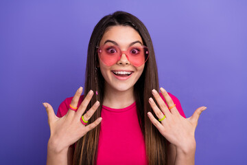 Smiling young woman in pink sunglass showing colorful rings on her hands against vibrant purple...