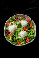 Fresh salad with mixed greens, shredded daikon radish, diced tomatoes, and cherry tomatoes in a white bowl on a black background.