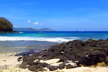 Empty tropical beach. Coastline with the sand and big stones. Exotic island shore with fisherman boat, sandy beach and blue ocean.