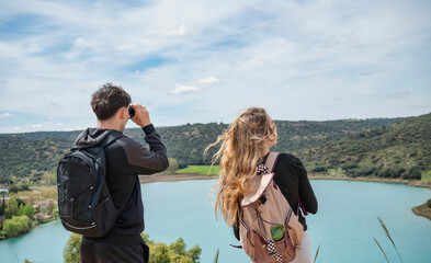 Young couple hiking and enjoying panoramic lake view with binoculars from mountain viewpoint