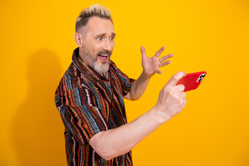 Middle aged man holding red smartphone on vibrant yellow background showcasing excitement and...