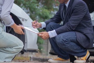 Confident male employee and female customer stand near damaged car, discussing repairs and...