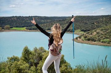 Teen girl pointing skyward with trekking pole while enjoying panoramic view of turquoise lagoon...