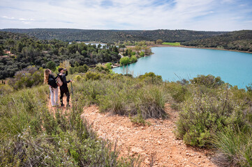 Teen boy and girl standing on a hillside trail overlooking a turquoise lagoon, exploring the landscape as the boy uses binoculars on a clear sunny day