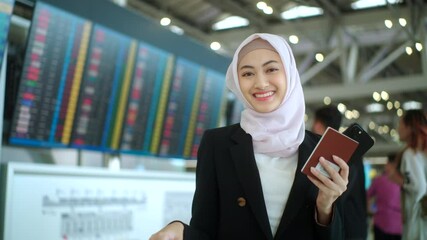 Happy asian muslim business woman wearing hijab holding smartphone and passport standing at airport terminal. Islamic woman people lifestyle travel. Muslim people concept.
 - Powered by Adobe