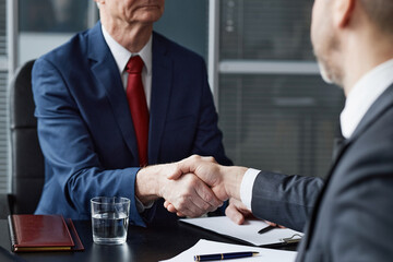 Middle aged Caucasian man in suit shaking hands with colleague during business meeting at office desk closing deal by signing documents at office