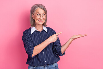 Confident mature woman pointing with one hand while smiling, styled against a vibrant pink...