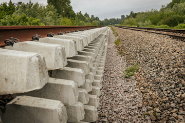 Layered concrete railway track sections are stacked beside an active rail line, viewed from the...