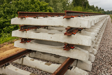 Neatly stacked concrete and steel railway track sections are positioned along an active railway...