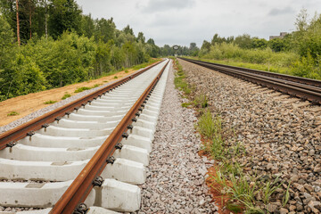 Obraz premium A curved section of newly laid railway track diverges beside an older line, with a circular signal sign and red light signal post in a green, forested area.