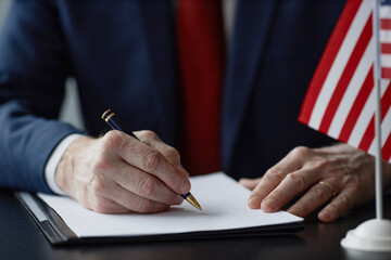 Close up on hands of Caucasian middle aged male official signing document at desk with American...