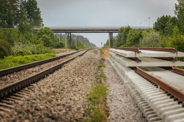 A close side view of stacked concrete railway track sections alongside a railway line, with a...