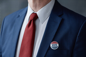 Cropped shot of Caucasian middle aged man wearing suit and red tie standing with vote badge pinned...