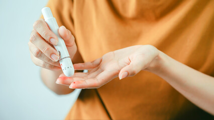 Close up of hand pricking fingertip with blood lancet device to measure glucose level for diabetes...