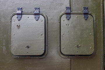 Green metal hatches with hinges on the armored body of a military truck, close up.
