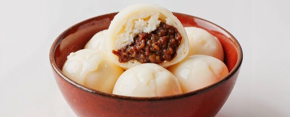 A delightful red bowl cradles several round dumplings, their smooth white exteriors contrasting with the rich brown filling peeking through one 